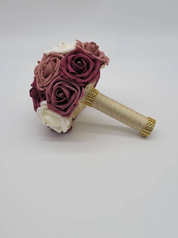 Dusty rose, mauve, burgundy, and ivory roses with rhinestones on every rose. Handle is made up of gold ribbon and gold bling wrap.