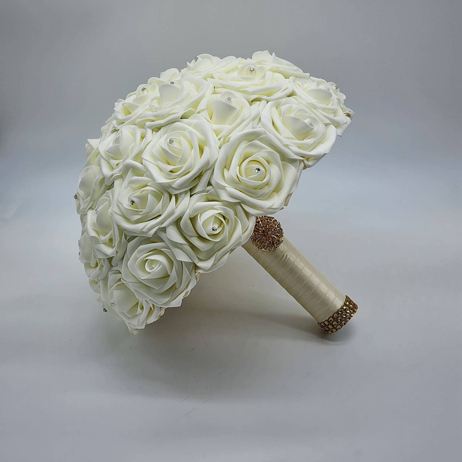 A ivory bridal bouquet made of foam roses with a satin ribbon and gold embellishments.