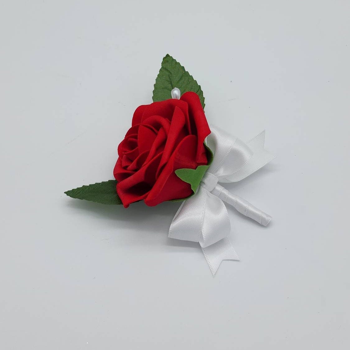 A single red rose with green leaves and a white satin ribbon, perfect for a wedding or special occasion.