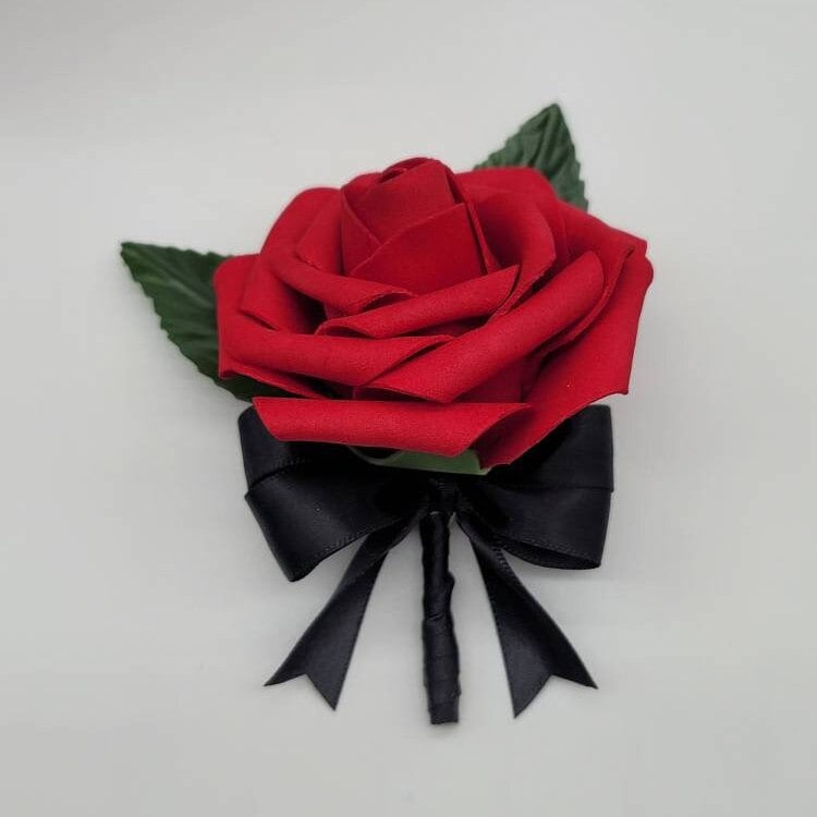 Red rose boutonniere with 2 green leaves, black satin ribbon. Flower is about 3 inches in diameter.
