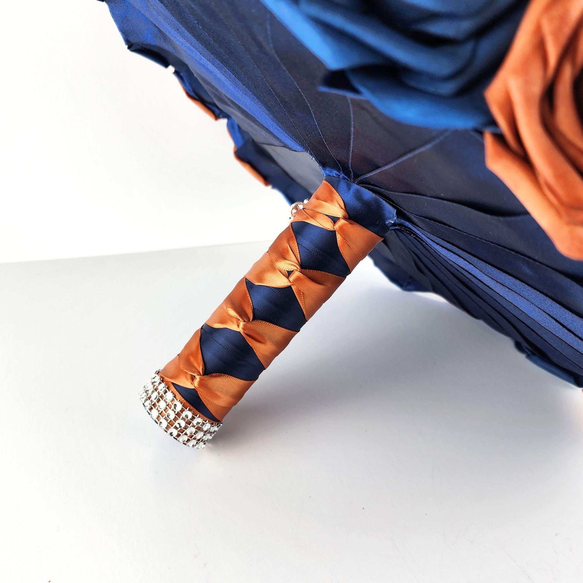 A navy blue and burnt orange real touch rose bridal bouquet with a crystal-embellished handle.
