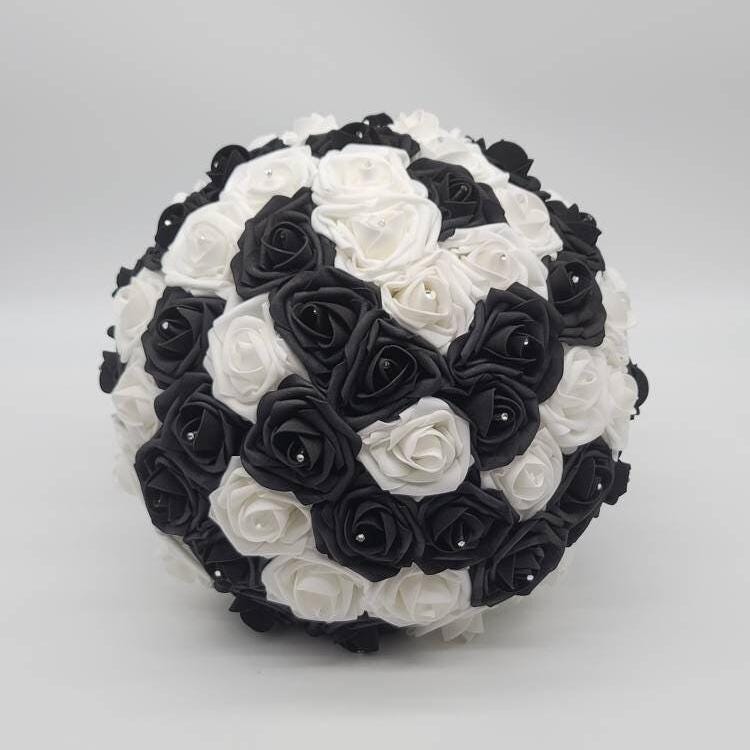 A round bouquet of artificial roses in a checkerboard pattern of black and white. Each rose is accented with a small, silver-colored bead in the center. The bouquet is set against a plain white background.