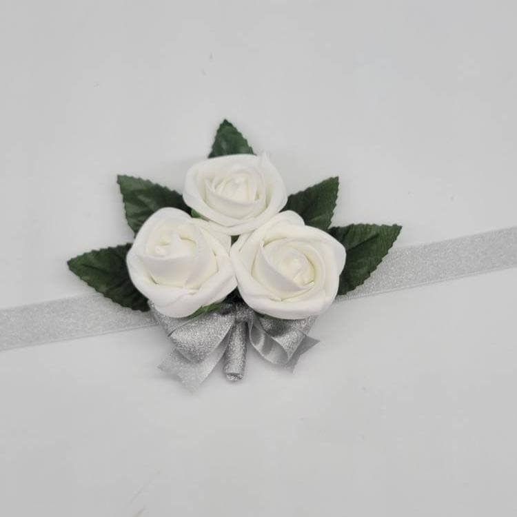 White wrist corsage with silver ribbon. flowers are 3 rose buds