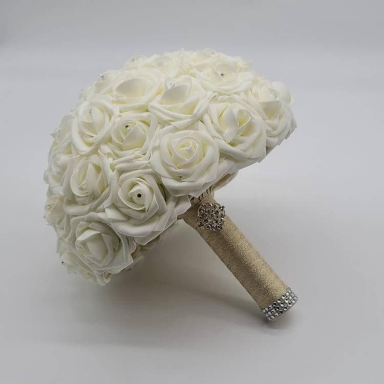 An Ivory bridal bouquet made of artificial roses with a rhinestone embellishment on the handle.
