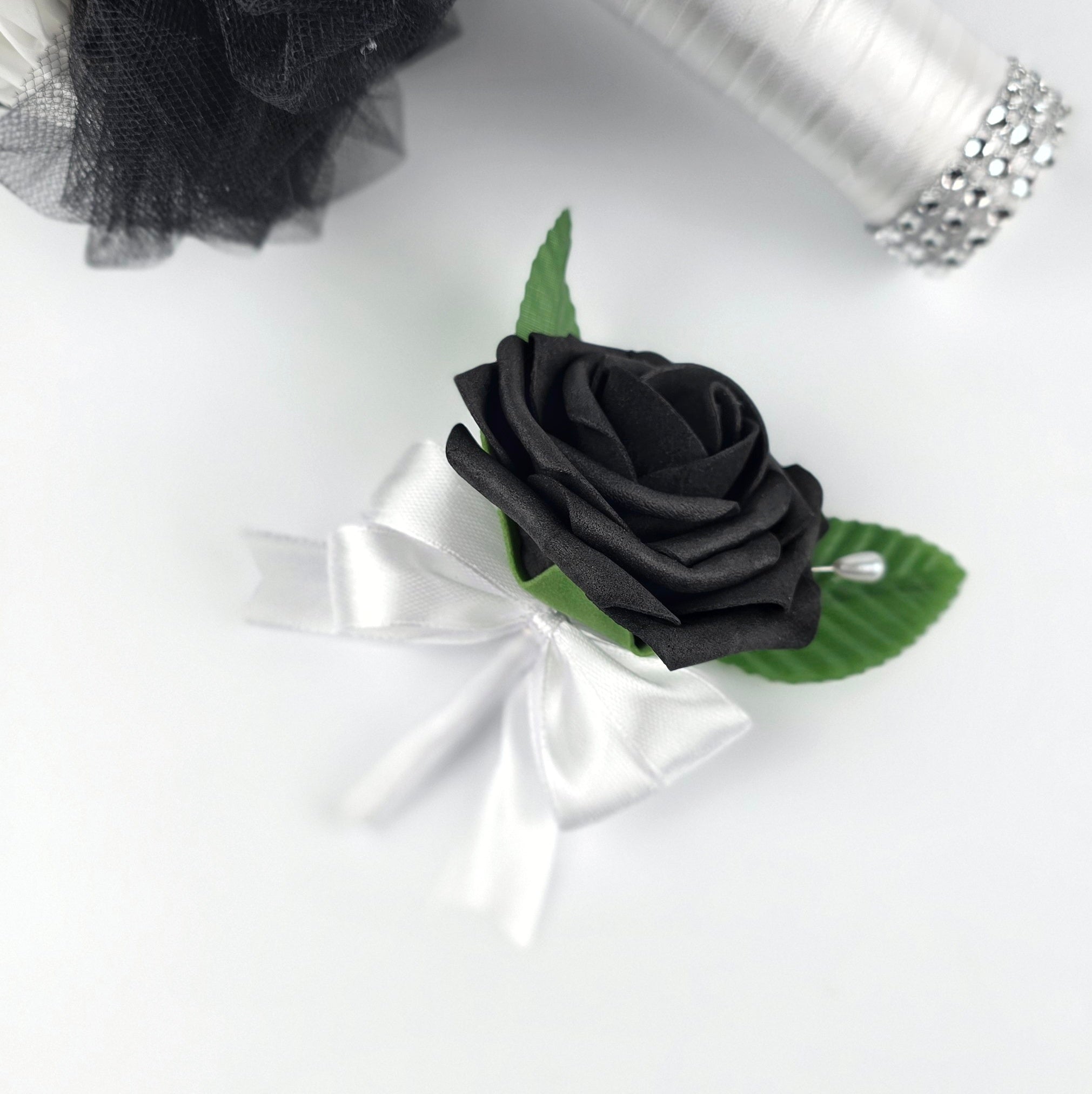 Black rose boutonniere with white ribbon, 2 green leaves, and a pearl pin