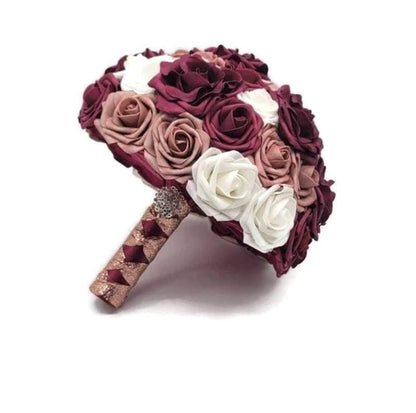 Burgundy, dusty rose, and white roses. Handle is made up of burgundy and rose gold ribbon in a French twist style and finished with a silver brooch.