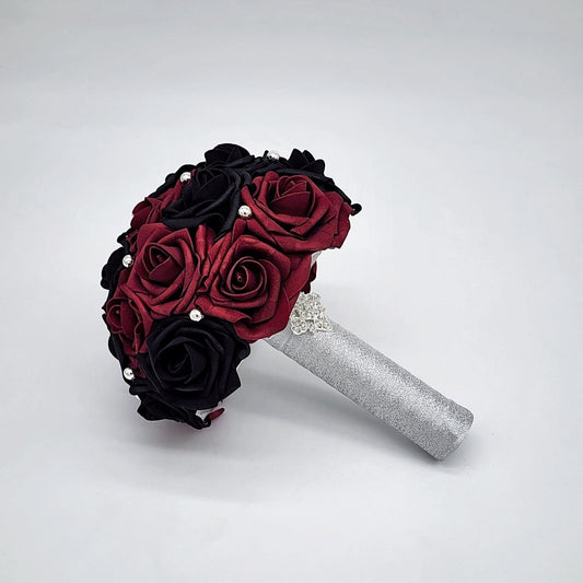 Burgundy and black wedding bouquet made with Real Touch Rose. Silver balls are scattered throughout bouquet. Handle is made with silver ribbon and finished with silver brooch.