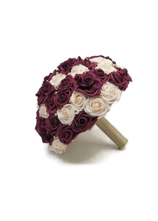 Burgundy and Cream Real Touch Roses with gold balls and avalanche roses scattered throughout. handle is made up of gold ribbon.