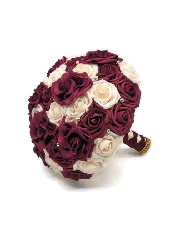 Burgundy and cream real touch rose bouquet. Burgundy Avalanche Roses scattered throughout as well as gold balls. Handle is made using ivory and Burgundy ribbon in French twist style