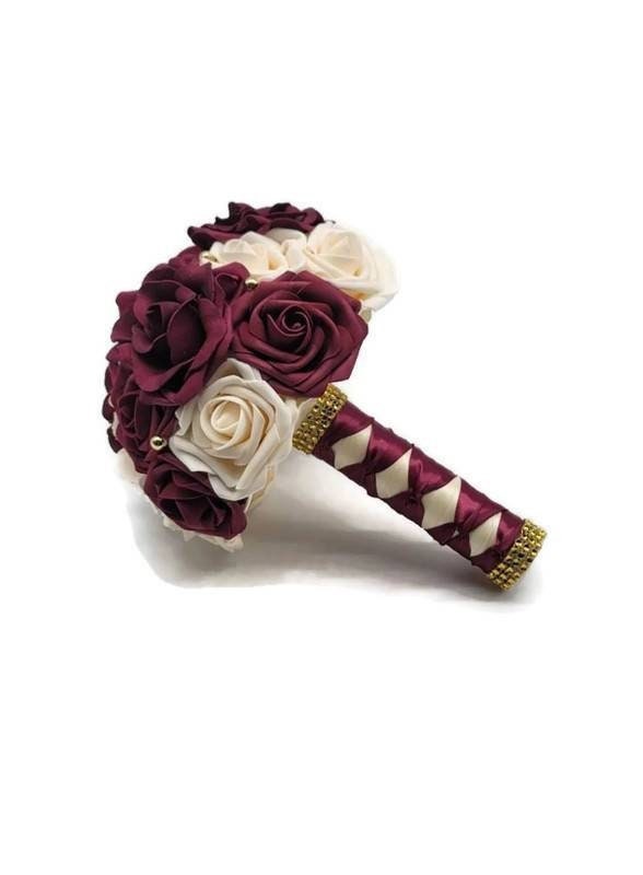 Burgundy and Cream bridal bouquet with avalanche roses and gold pearls scattered throughout. Handle is made up of ivory and burgundy ribbon in a French twist style and finished off with gold bling wrap.