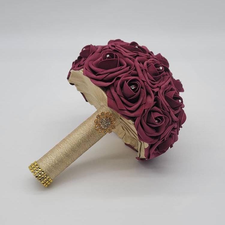 Burgundy and gold wedding bouquet made with RealTouchRose. Rhinestonesare in the center of every rose. Handleis made using Gold ribbon and finished with Goldbrooch and bling wrap.