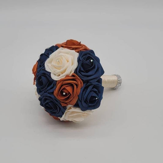 Burnt orange, cream, and navy rose bouquet with rhinestones on every rose. Handle is made up of ivory ribbon and finished with silver bling wrap.