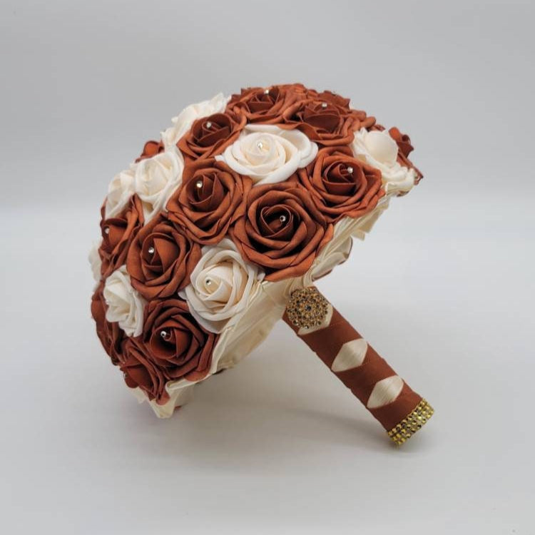 Burnt orange and cream roses with rhinestones on every rose. handle is made up of burnt orange and ivory ribbon in a french twist style and finished with gold brooch and bling wrap.