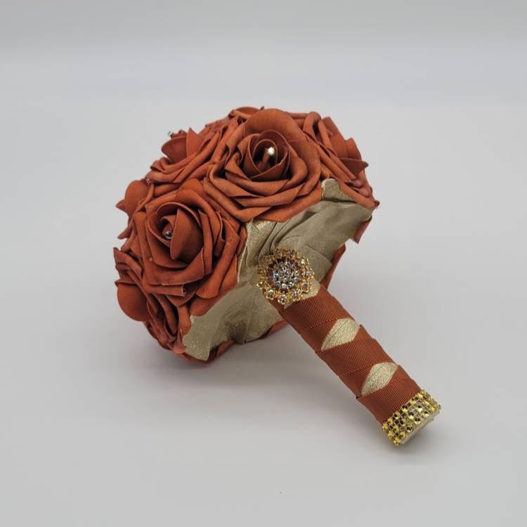 Burnt orange rose bouquet with handle wrapped in gold and burnt orange ribbon and finished with gold brooch and bling wrap. Rhinestones on every rose.