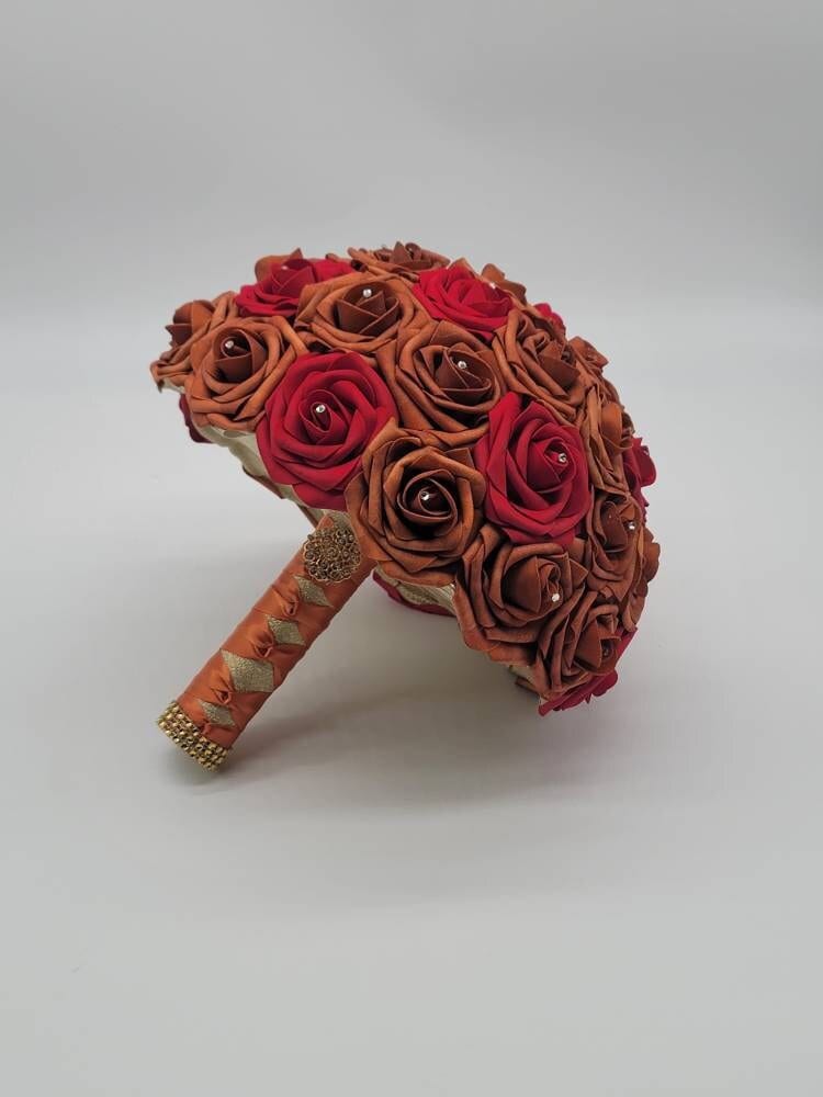 Burnt orange and red rose bouquet with rhinestones on every rose. handle is made up of burnt orange and gold ribbon and finished with a gold brooch and gold bling wrap.