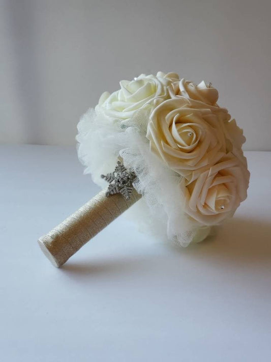 Cream bridal bouquet made with real touch roses with ivory tulle. Handle is made using gold ribbon and snowflake brooch.