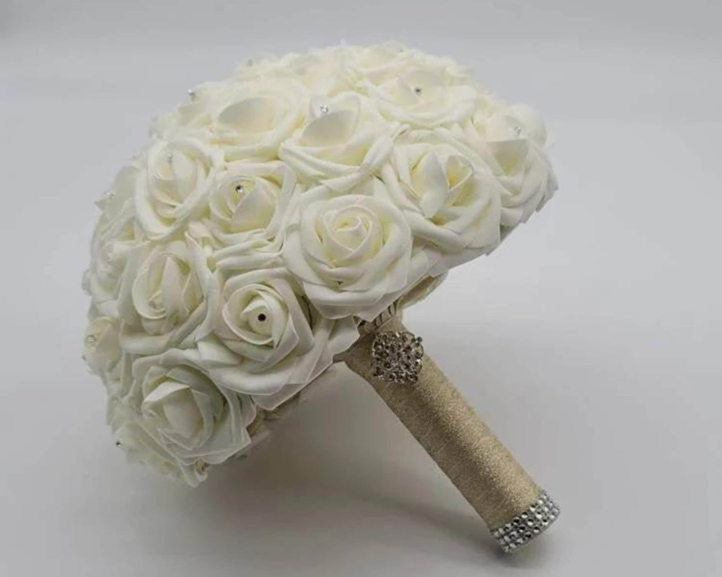 Ivory rose wedding bouquet with gold ribbon and finished with silver brooch and bling wrap. Every rose has a rhinestone on it.