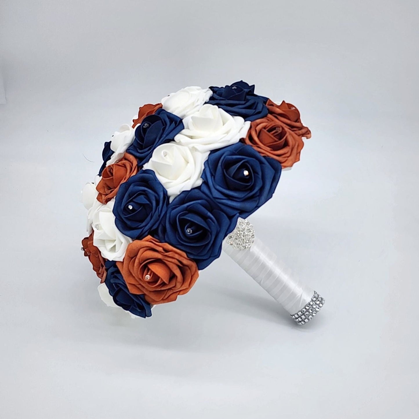 burnt orange, navy, and white bouquet with rhinestones on every rose. handle is made up of white satin ribbon and finished with silver brooch and bling wrap.