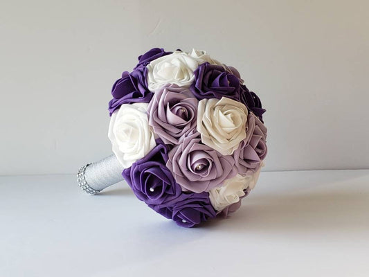 lilac, purple, and white bridal bouquet made with real touch roses. rhinestones are in the center of every rose. Handle is made with silver ribbon and finished with silver bling wrap.