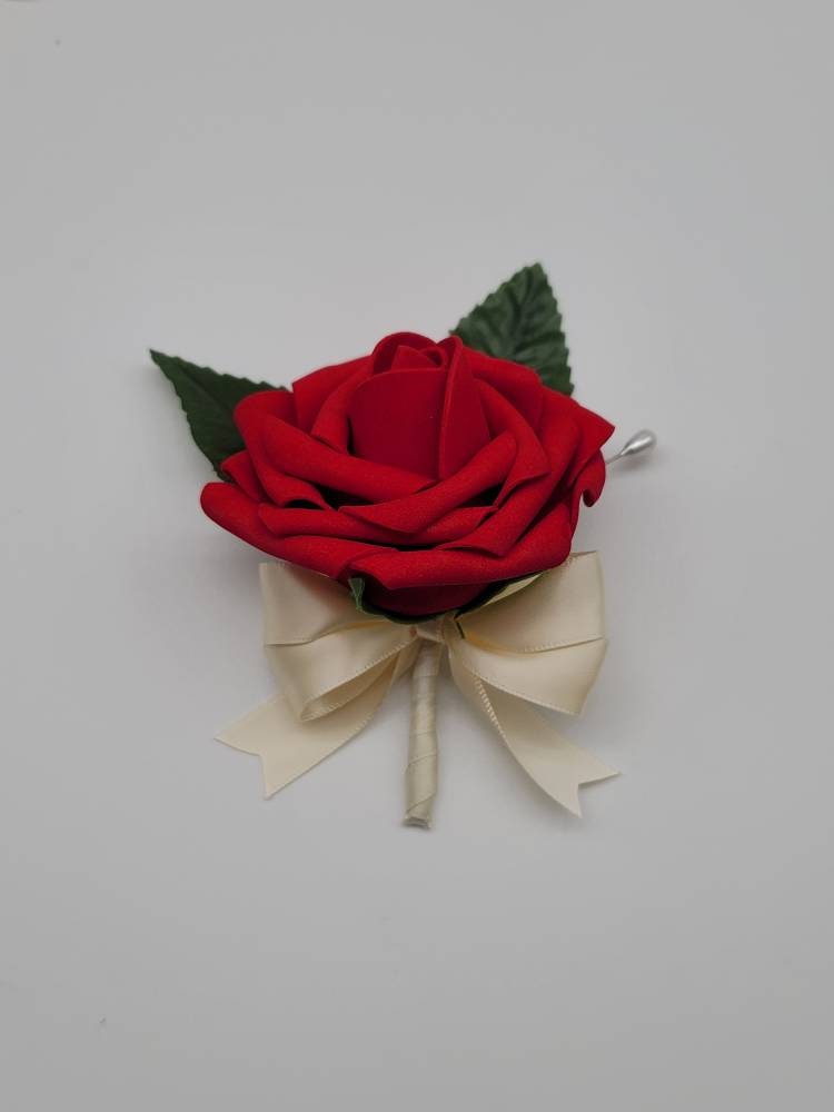 Red boutonniere with real touch roses and ivory satin ribbon. Pearl pin and faux leaves used