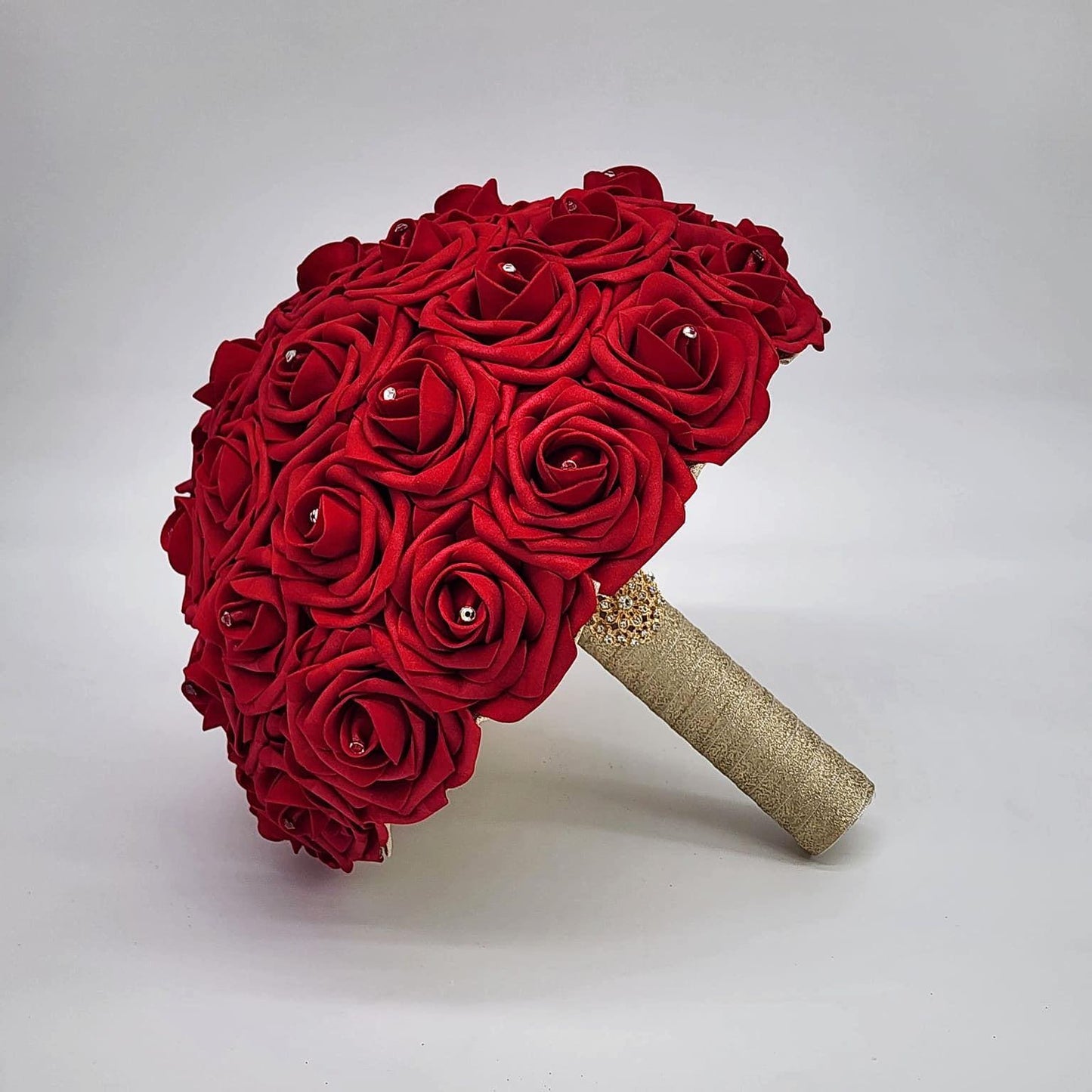 Red wedding bouquet made with real touch roses. Handle is made using gold ribbon and finished with a gold brooch. Rhinestones are on every rose.