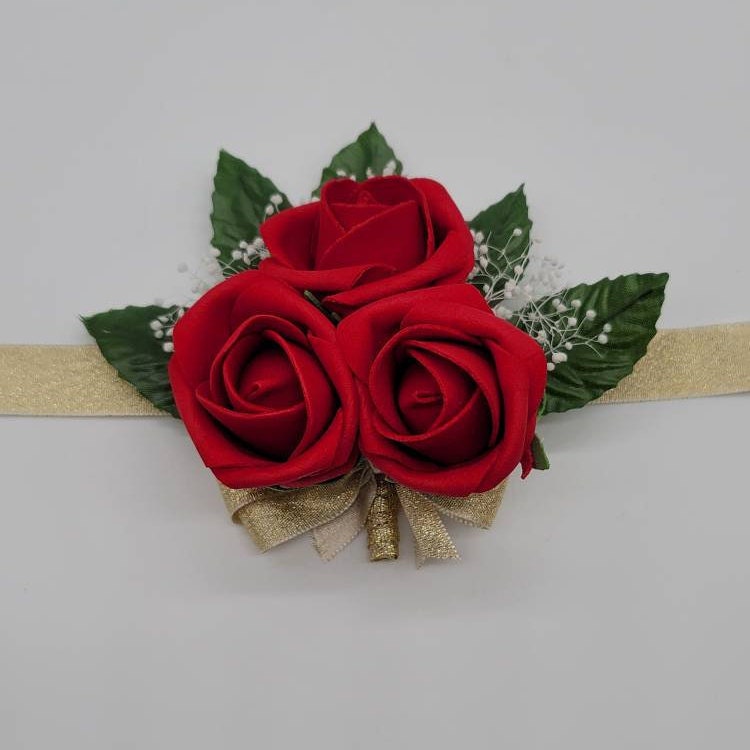 Red wrist corsage made with Real Touch roses. 3 small rose buds and 5 faux leaves. Baby&#39;s breath behind the roses. Gold ribbon and gold ribbon wrist tie.