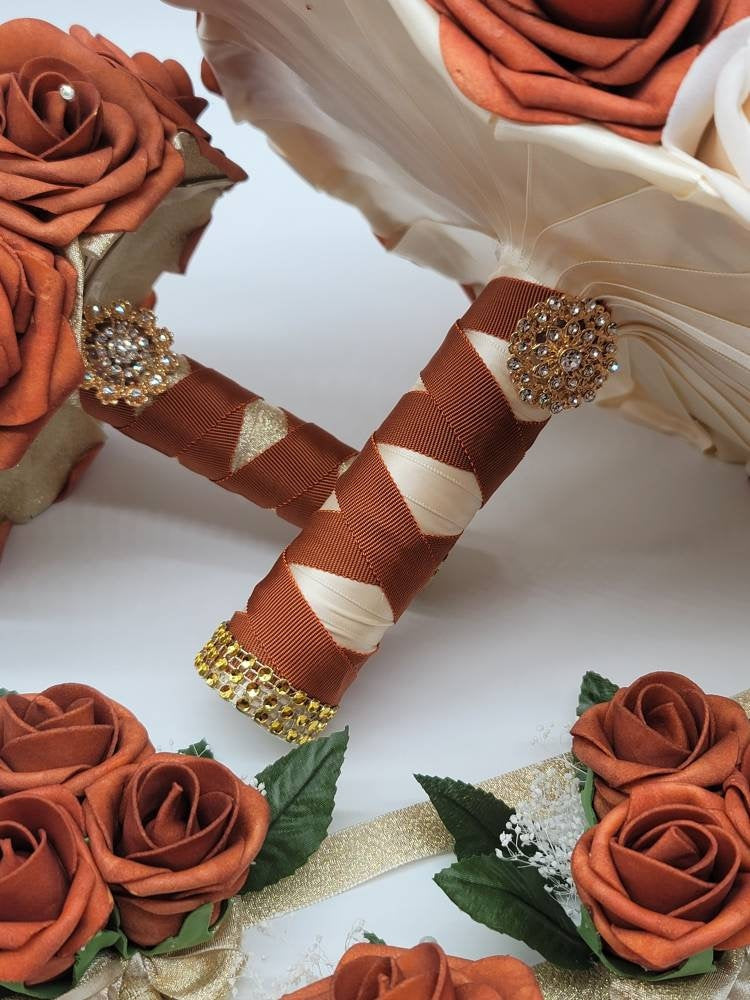 Three bouquets of faux flowers with burnt orange and cream roses and gold ribbon. The bouquets are tied with burnt orange ribbon and embellished with rhinestones.