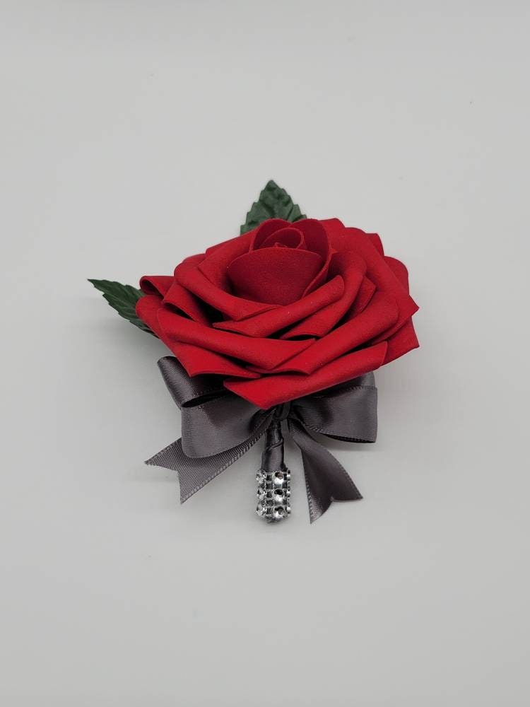 Red rose boutonniere made with real touch roses. gray satin ribbon and a strip of bling wrap on handle. Faux leaves and pearl pin