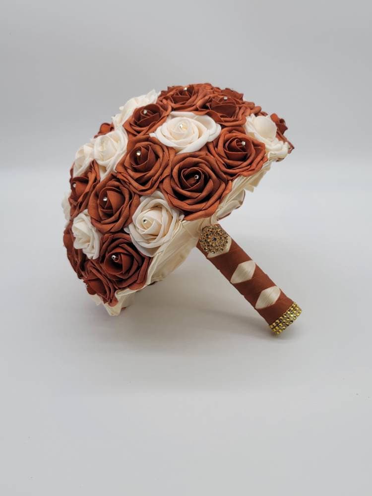Burnt orange and cream roses with rhinestones on every rose. handle is made up of burnt orange and ivory ribbon in a french twist style and finished with gold brooch and bling wrap.