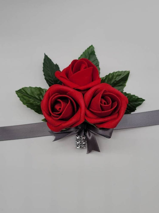 Red rose wrist corsage with 3 red rose buds and faux leaves. Ribbon is satin gray with a strip of bling wrap on stem.