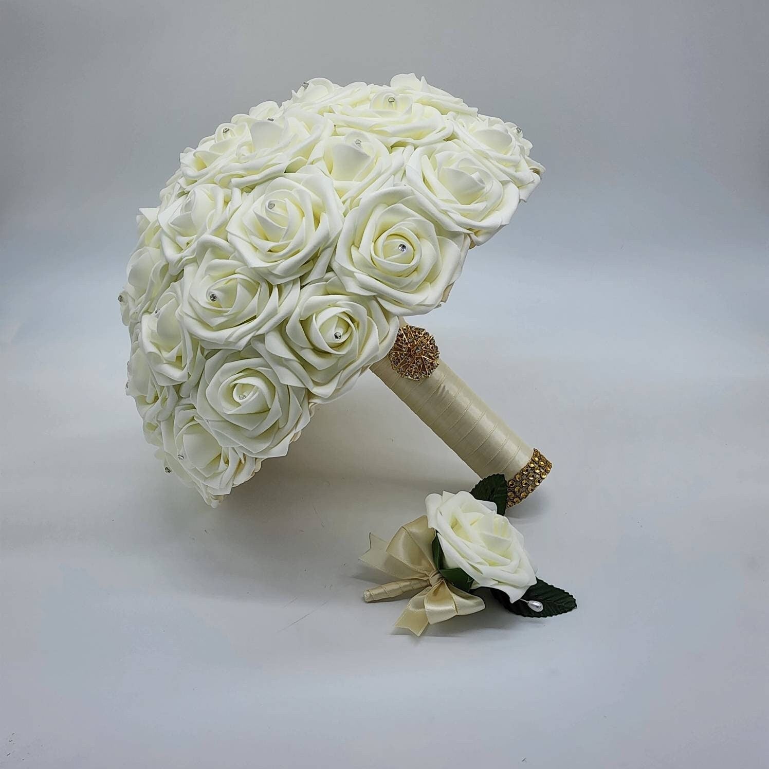 A ivory bridal bouquet made of artificial roses with a ivory ribbon and a matching boutonniere.