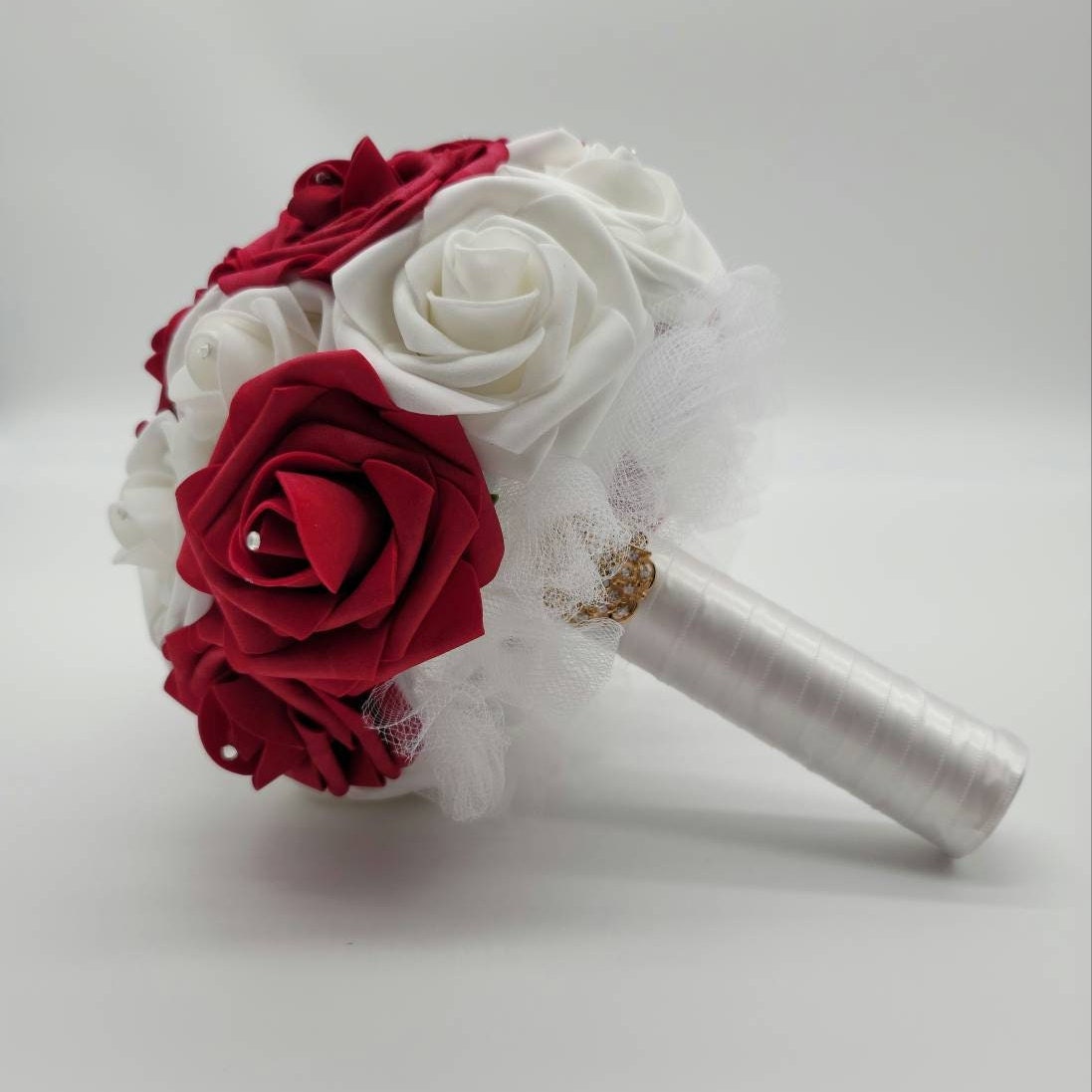 A white and red bridal bouquet with white tulle and a white satin ribbon handle.
