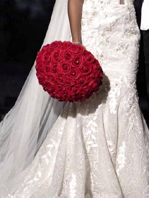 Bride in white dress holds on her side a Red real touch rose bouquet with black satin ribbon handle. Silver bling wrap on handle. Rhinestones on every rose.