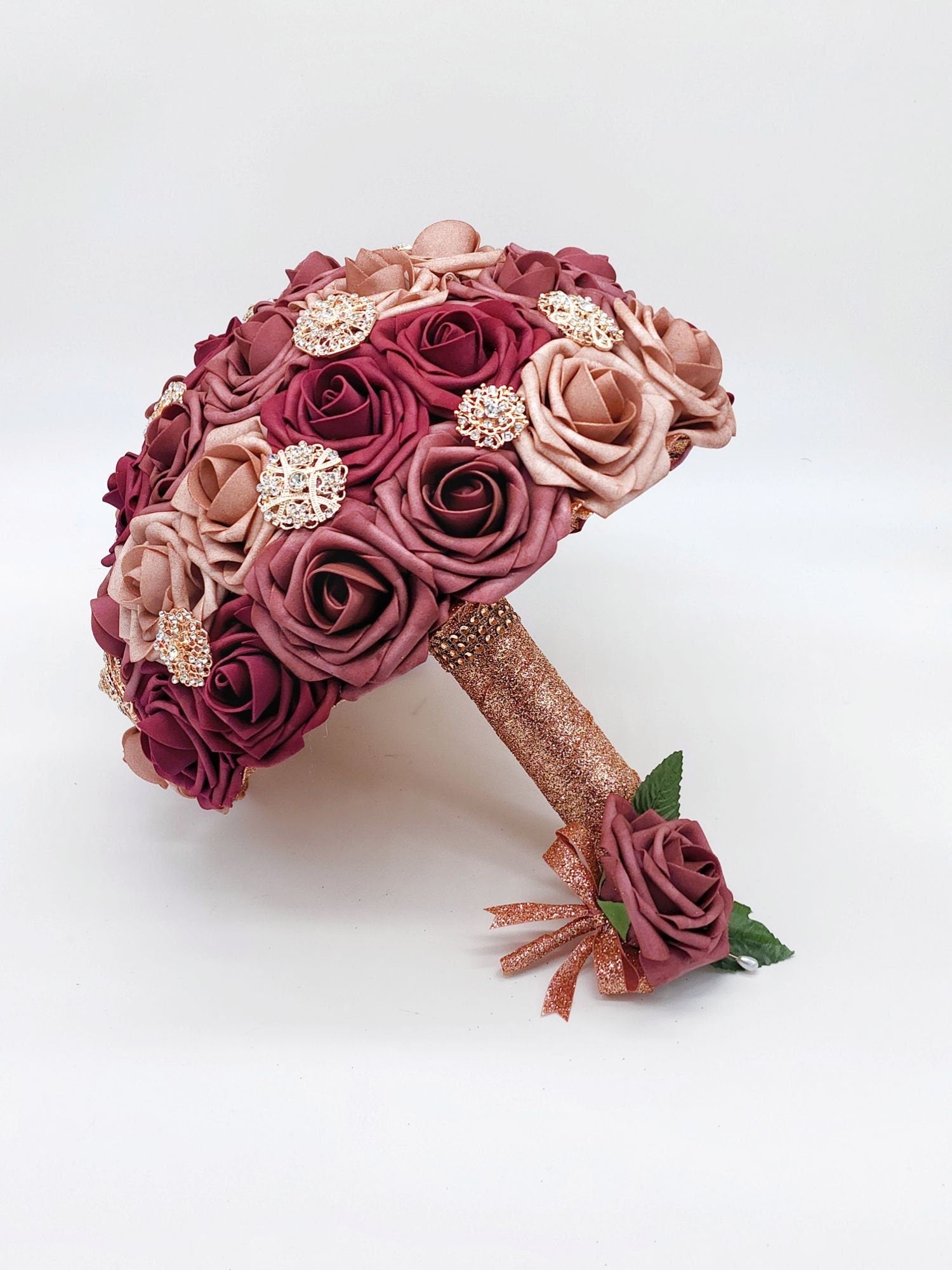 Dusty rose, burgundy, and mauve bridal bouquet with rose gold ribbon. Rose gold brooches are scattered throughout bouquet. Matching mauve boutonniere with rose gold ribbon.