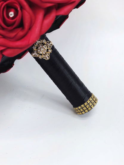 Close up of handle. Red real touch rose bouquet with black satin ribbon handle. Gold bling wrap and brooch on handle. Rhinestones on every rose.