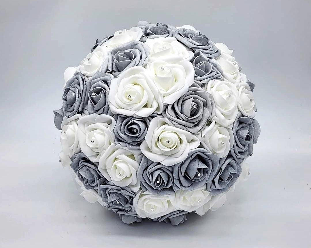 A round bridal bouquet made of white and silver artificial roses. The bouquet is decorated with small, sparkly rhinestones.