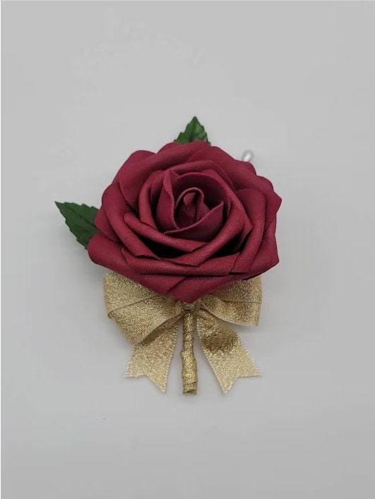 Shows matching Boutonniere. Burgundy rose and gold ribbon with bow