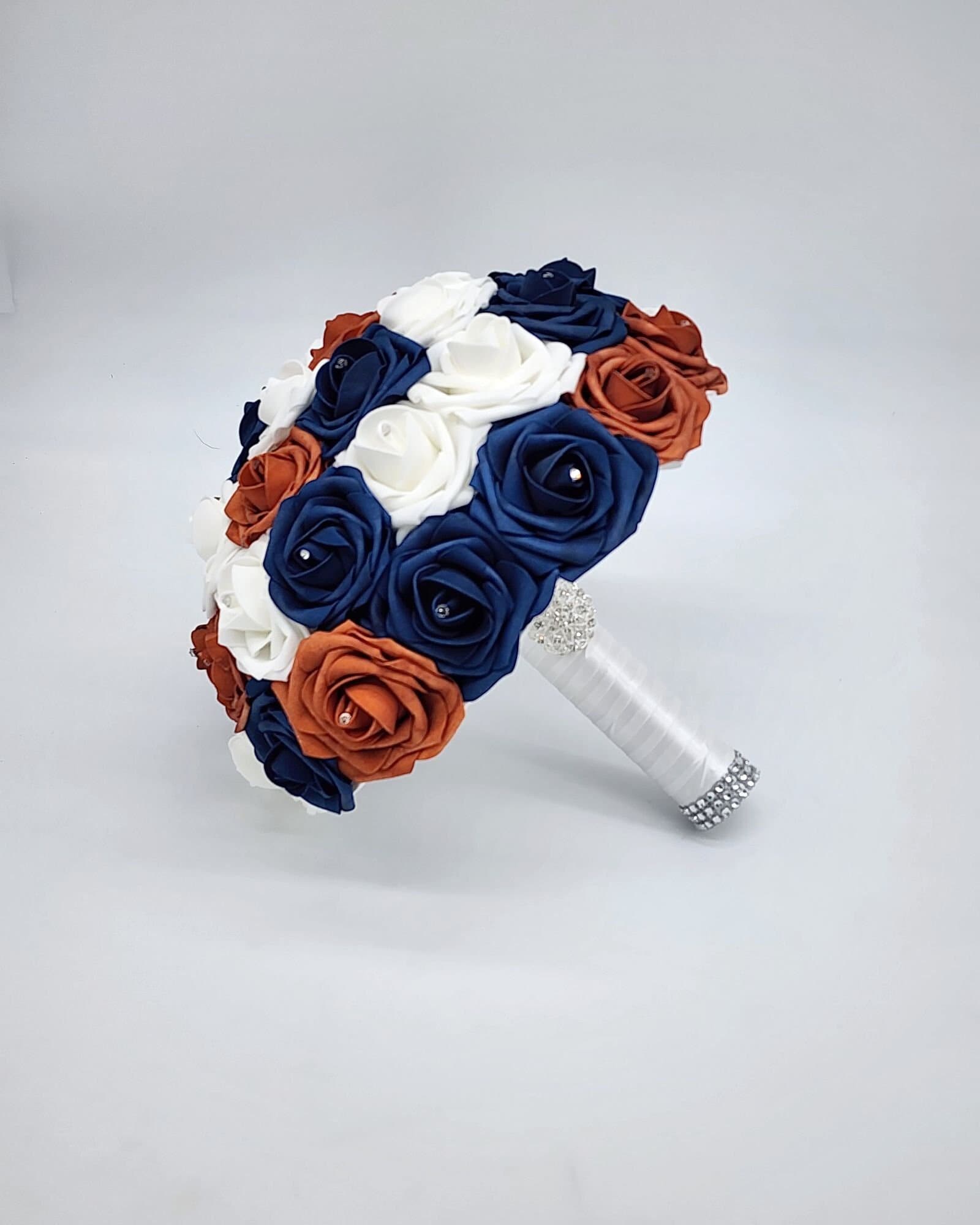 burnt orange, navy, and white bouquet with rhinestones on every rose. handle is made up of white satin ribbon and finished with silver brooch and bling wrap.