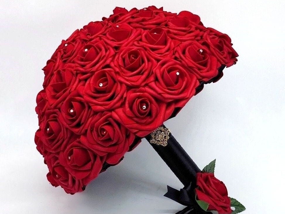 Red Real Touch Roses Wedding Bouquet with Black Satin Ribbon handle. Handle is finished with a gold brooch and gold bling wrap. Rhinestones are on every rose. Red rose boutonniere with black satin ribbon with pearl pin.