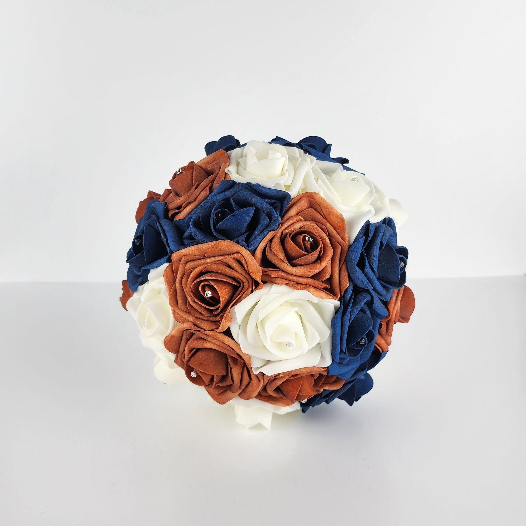 A round bouquet of artificial flowers in shades of ivory, burnt orange, and navy blue. The flowers are arranged in a circular pattern and have a satin-like finish.