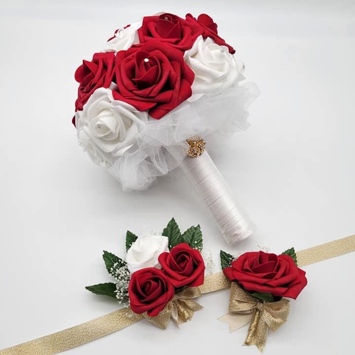 A bridal bouquet with red and white roses, a matching boutonniere, and a wrist corsage. The bouquet is wrapped in white tulle and has a gold accent. The boutonniere and corsage are tied with gold ribbon.