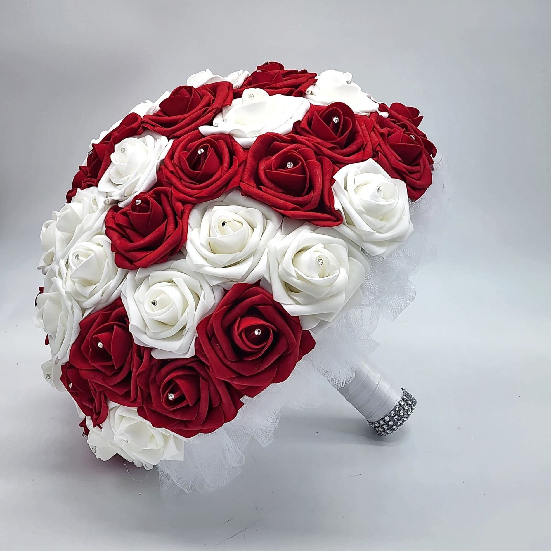 A bridal bouquet made of red and white artificial roses with a white tulle and satin ribbon wrap.