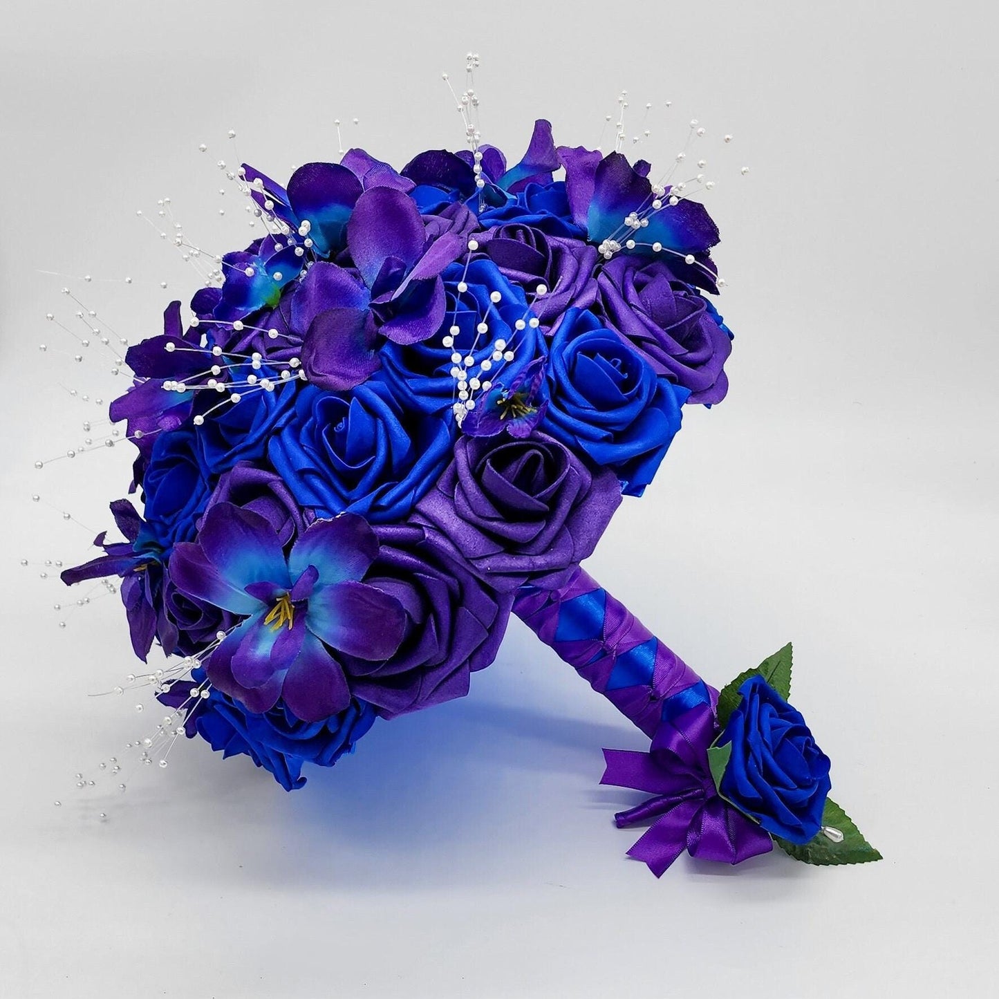 Purple and royal blue roses with galaxy orchids and pearl spay scattered throughout. Handle is made out of royal blue and purple ribbon in a French twist style.