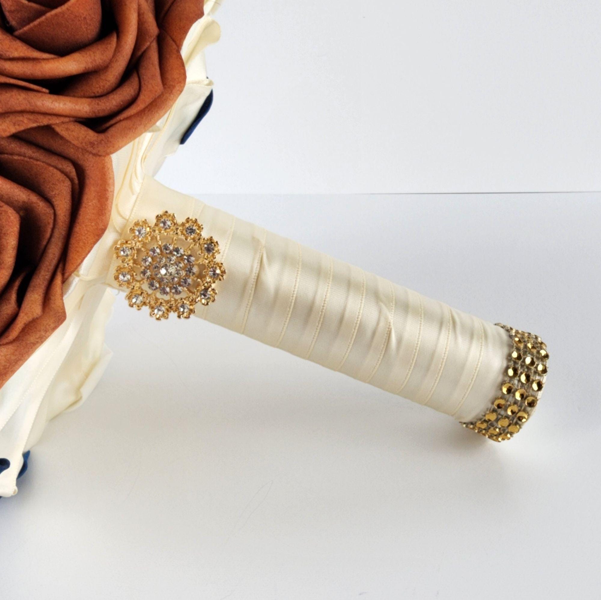 A bridal bouquet with ivory and burnt orange roses, accented with a gold rhinestone brooch and a gold rhinestone trim on the handle.