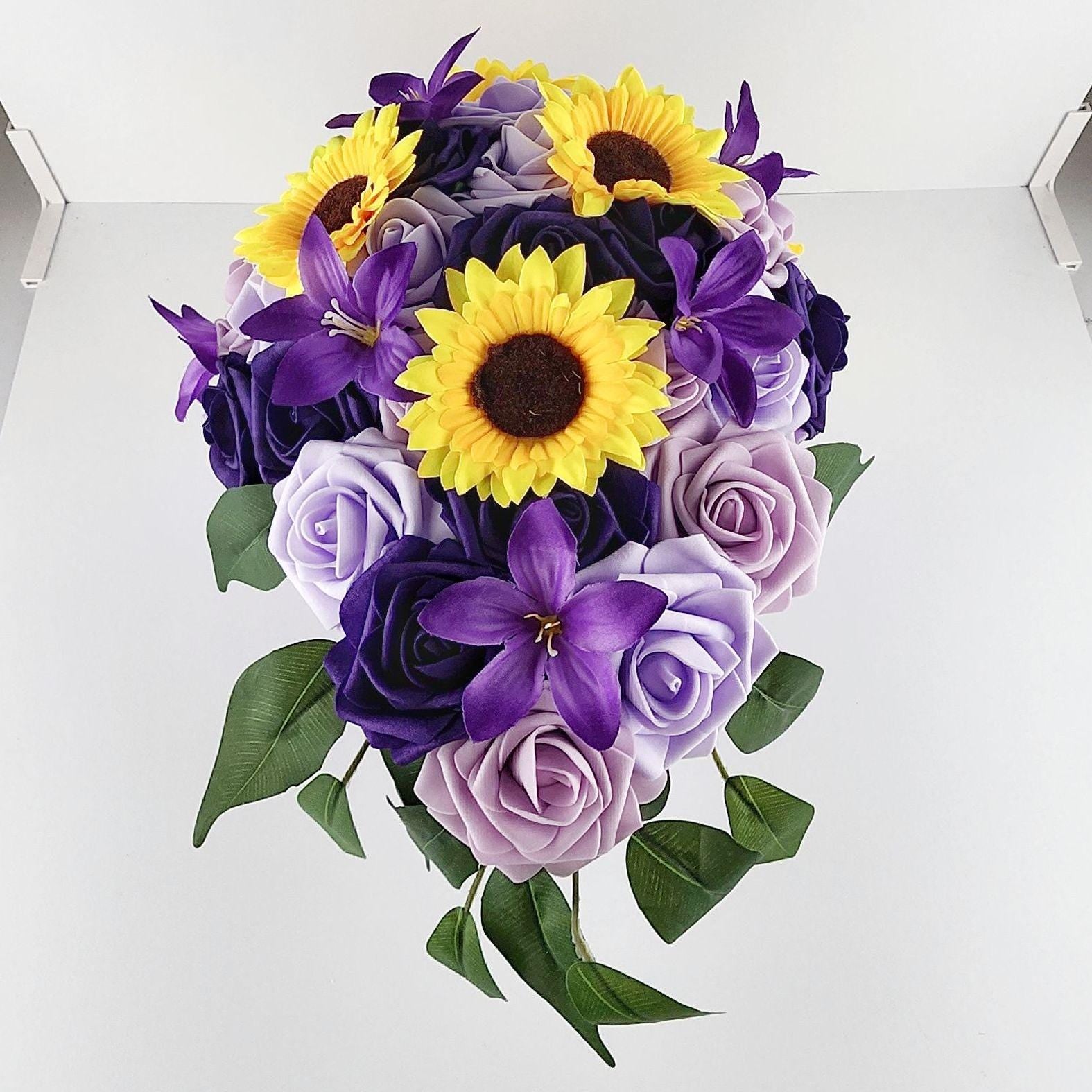 Close up front view of bouquet. Purple flowers of different shades scattered in a tear drop shape.