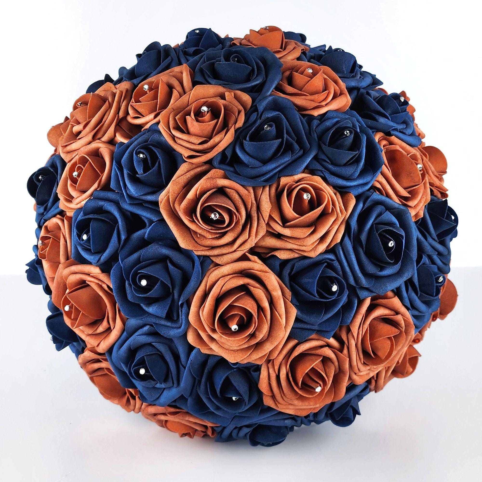 A round bouquet of artificial roses in navy blue and burnt orange colors. The roses are arranged in a circular pattern, with the navy-blue roses on the outside and the burnt orange roses on the inside.