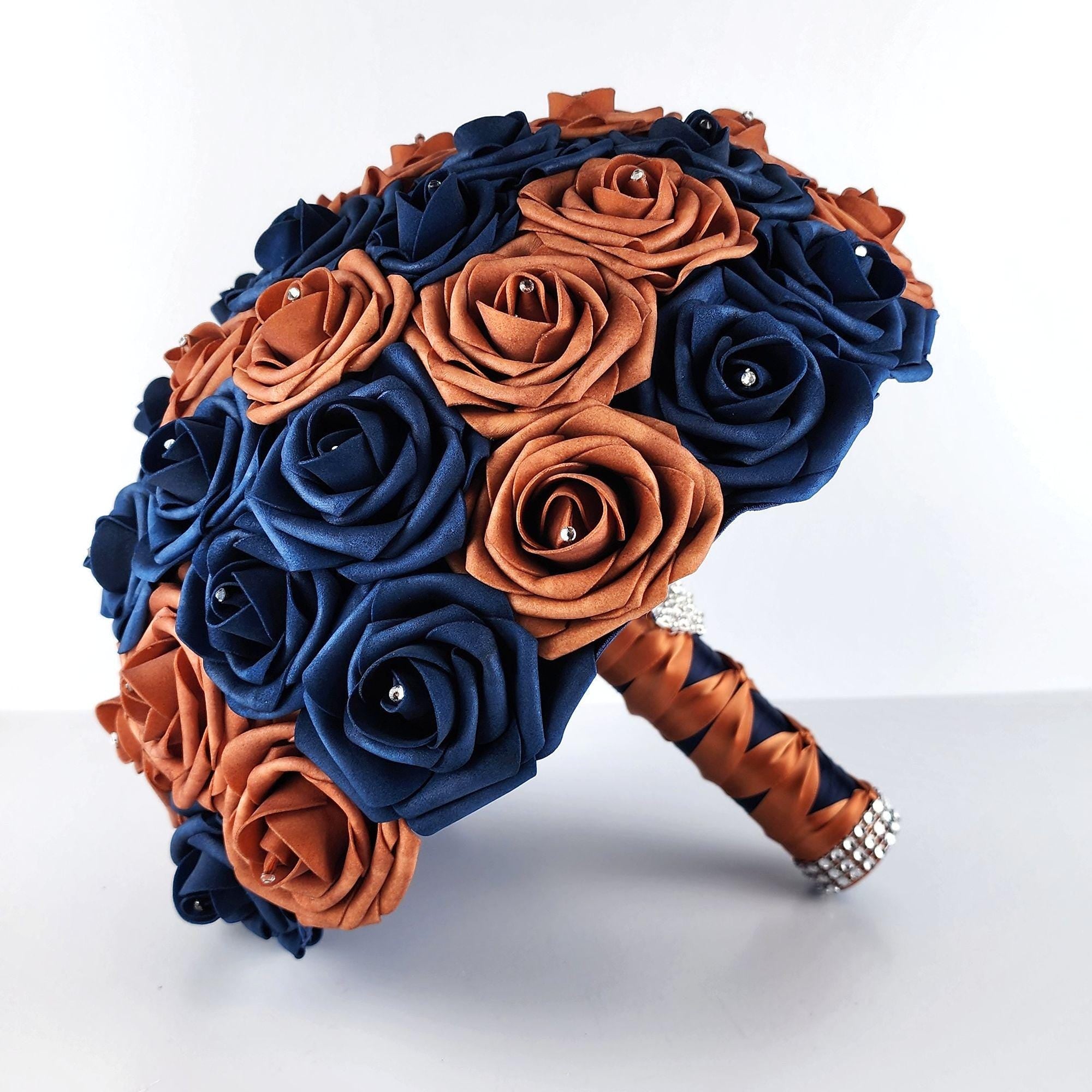 A bridal bouquet made of navy blue and terracotta satin roses. The bouquet is tied with a burnt orange and navy satin ribbon and has a rhinestone embellishment.