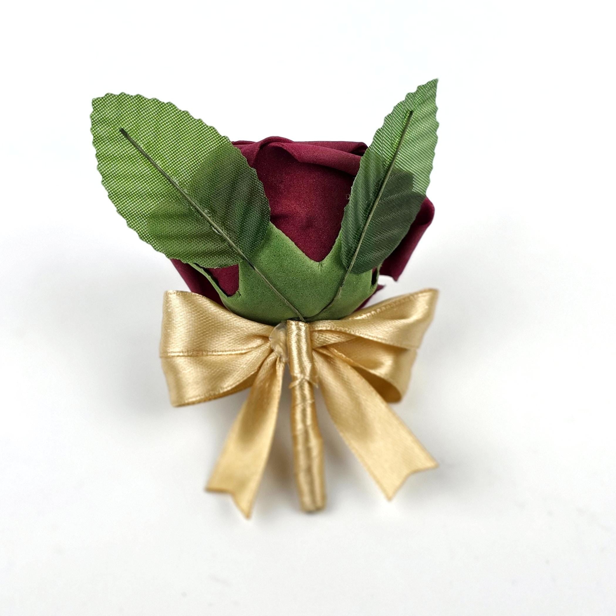 A burgundy rose boutonniere with green leaves and a gold satin bow. The artificial flower is a classic accessory for formal events, adding a touch of elegance.