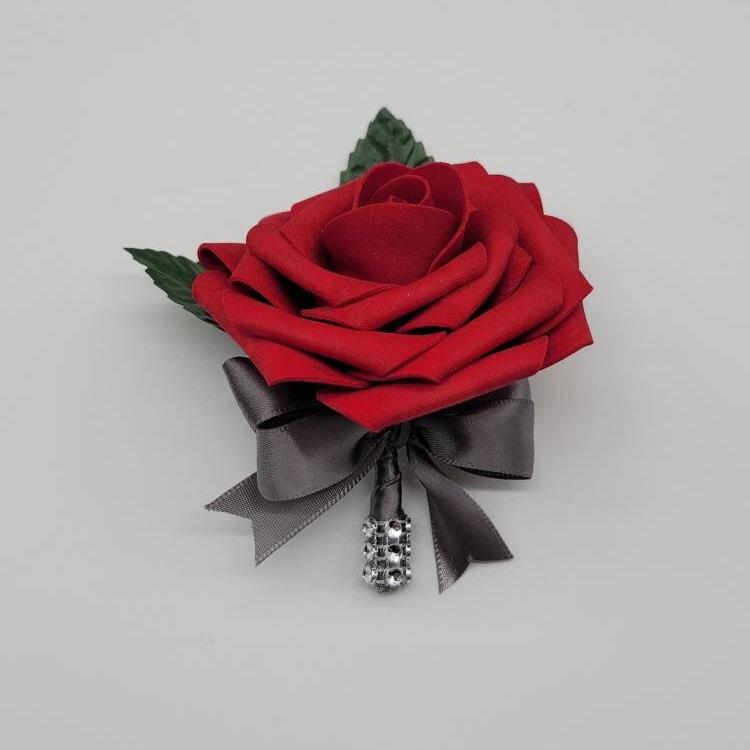 Red rose boutonniere made with real touch roses. gray satin ribbon and a strip of bling wrap on handle. Faux leaves and pearl pin