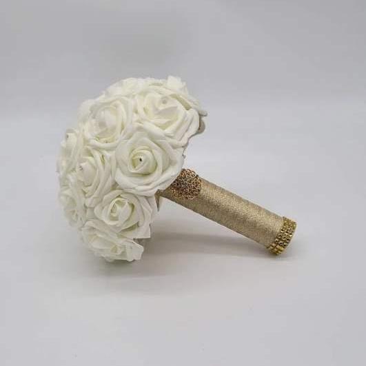 A Ivory bridal bouquet made of artificial roses with a gold glitter wrapped stem and a rhinestone embellishment.